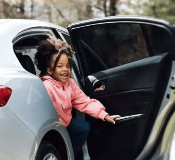 Smiling child safely exiting a car during school pickup using Kidz and Keyz digital afterschool dismissal platform for Charleston schools